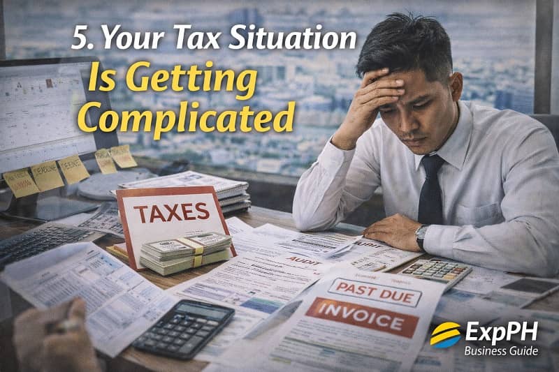 Filipino entrepreneur stressed while reviewing tax documents, invoices, and financial records, representing complex tax responsibilities in the Philippines